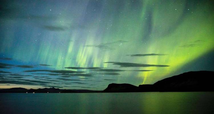 Les rideaux d'aurores boréales se reflètent sur un lac islandais calme la nuit.