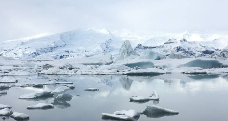 Des icebergs et des pics enneigés se reflétant dans les eaux calmes d'un lagon glaciaire.