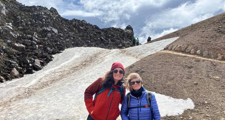 Deux randonneurs posent à côté d'une plaque de neige estivale sur une pente rocheuse.