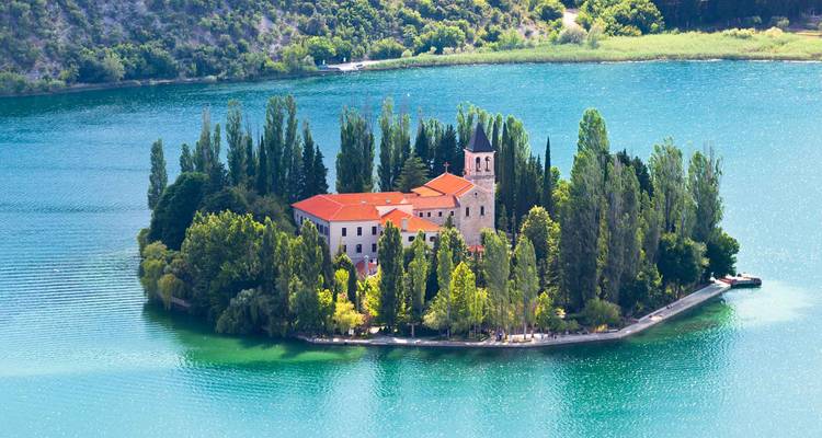 Petite île verdoyante avec monastère et cyprès entourés par un lac d'un bleu éclatant