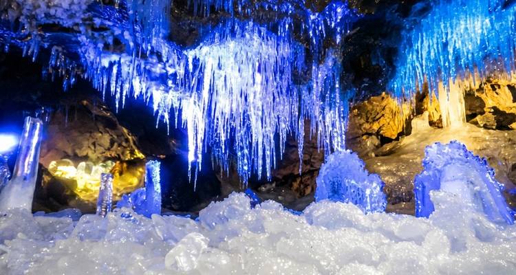 Glitzernde blaue Eiszapfen und gefrorene Formationen in einer beleuchteten Eishöhle.
