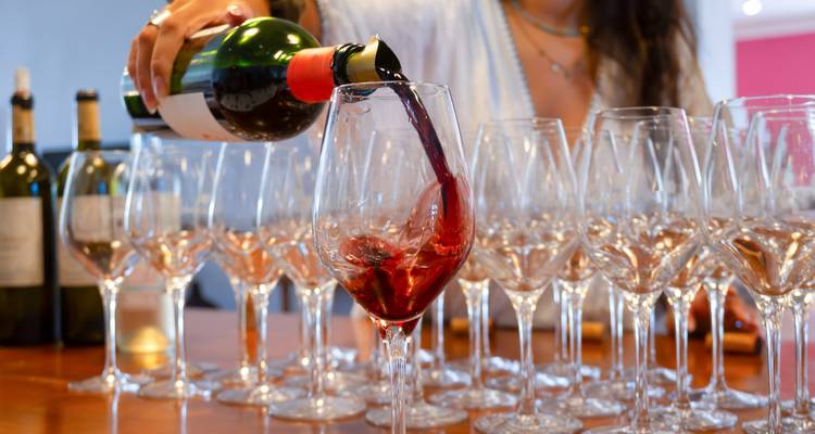 Hand die levendige rode wijn in een glas giet, netjes uitgestald met veel lege glazen voor de proeverij.