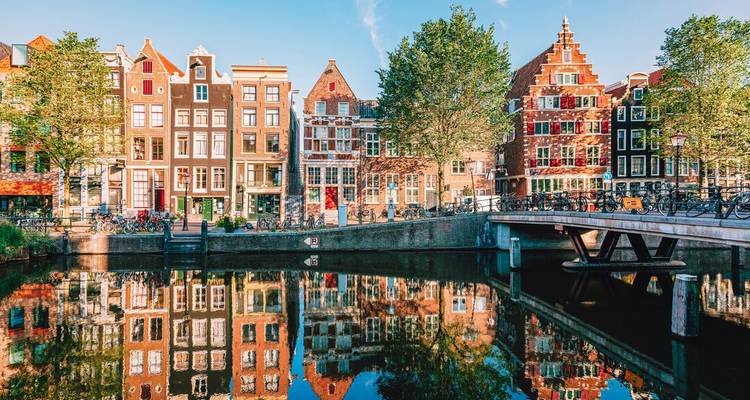 De trapgevelhuizen van Amsterdam spiegelen zich perfect in het stilstaande water onder een heldere blauwe hemel.