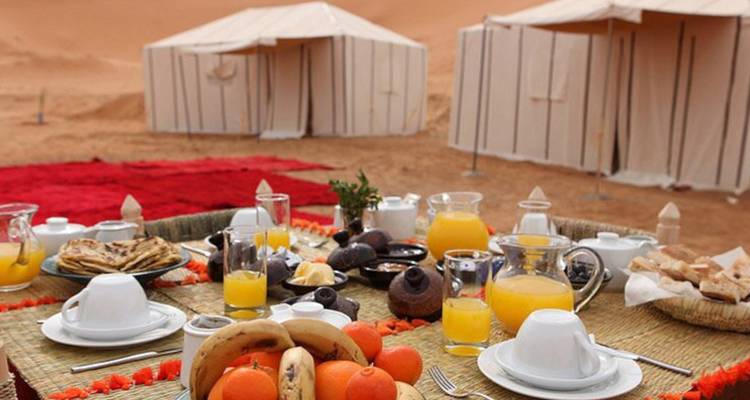 Buffet de petit-déjeuner traditionnel avec jus et fruits disposés sur une table basse devant les tentes du désert.