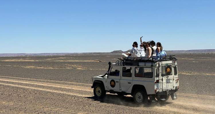 Toeristen rijden bovenop een witte Land Rover en jagen stofwolken op door de immense Marokkaanse woestijn.