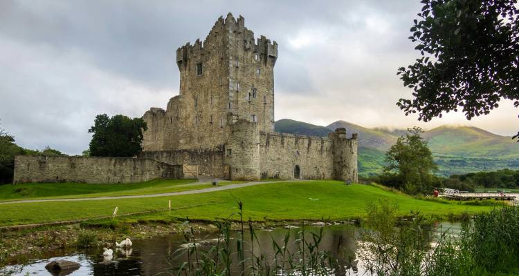 El Castillo Medieval de Ross reflejado en un lago tranquilo rodeado de colinas verdes.