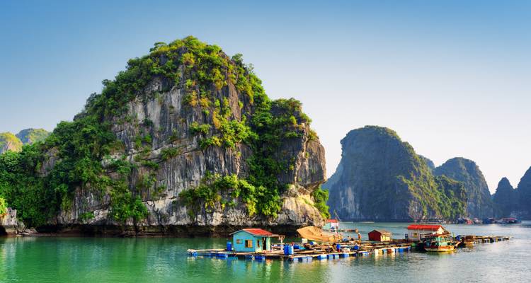 Emerald waters and towering limestone karsts surround a floating village in Ha Long Bay under a clear sky.