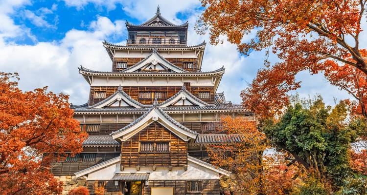 Château japonais traditionnel encadré par un feuillage automnal rouge vif sous un ciel bleu brillant.