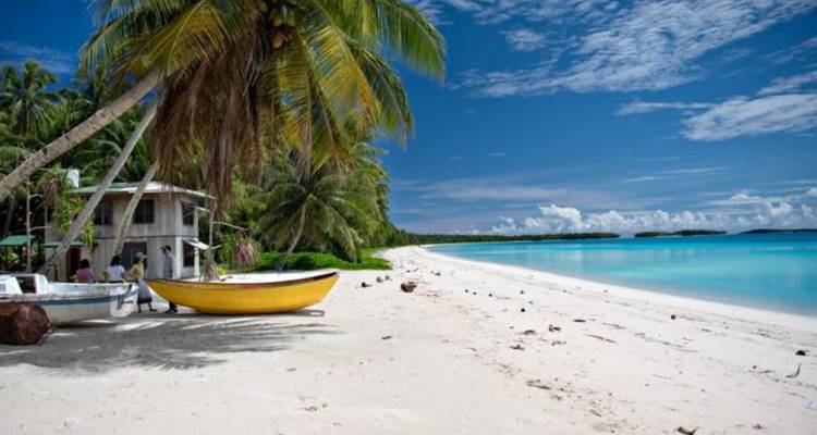 Palmbomen omzoomd wit strand met bootjes rustend op poederachtig zand onder verspreide wolken.