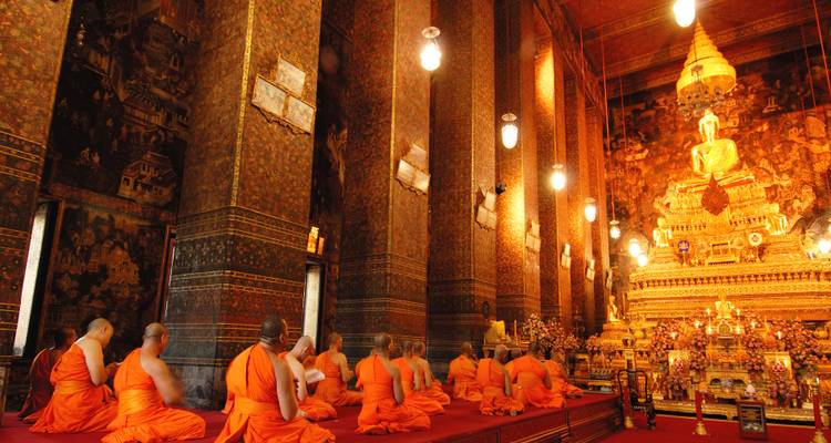 Reihe von buddhistischen Mönchen in orangefarbenen Roben, die in einer aufwändig dekorierten Tempelhal beten