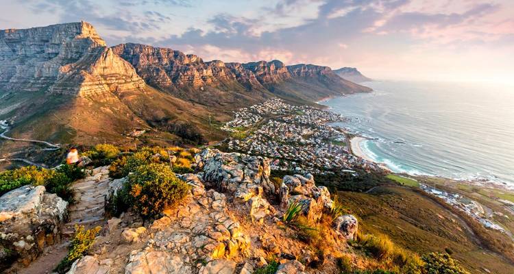 Panoramablick auf den Sonnenuntergang über die Camps Bay von Kapstadt und die Berge der Zwölf Apostel von einem felsigen Wanderweg aus.