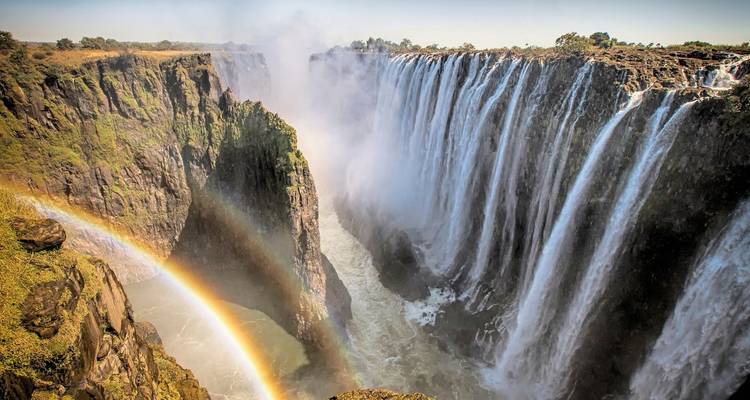 Les majestueuses chutes Victoria se précipitant dans les gorges avec un double arc-en-ciel s'arquant à travers la brume qui s'élève.