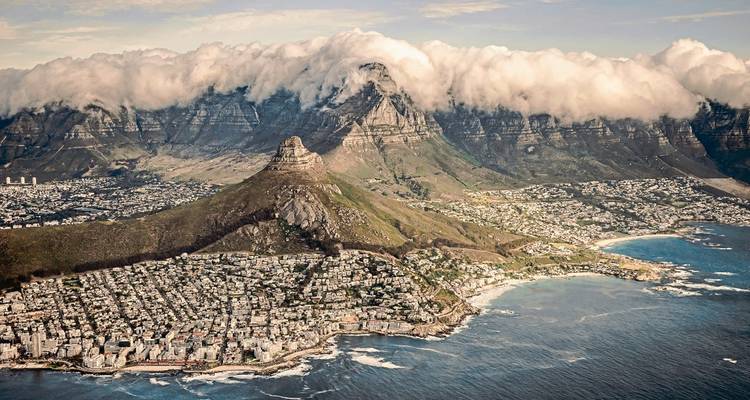 Aerial view of Cape Town with Lion’s Head and cloud-capped Table Mountain looming over the city and coast.