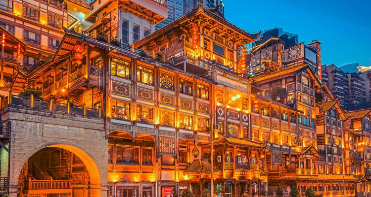 Beleuchtete traditionelle Berggebäude mit leuchtend orangen Lichtern vor einem tiefblauen Abendhimmel, das den Hongyadong-Komplex von Chongqing zur Schau stellt.