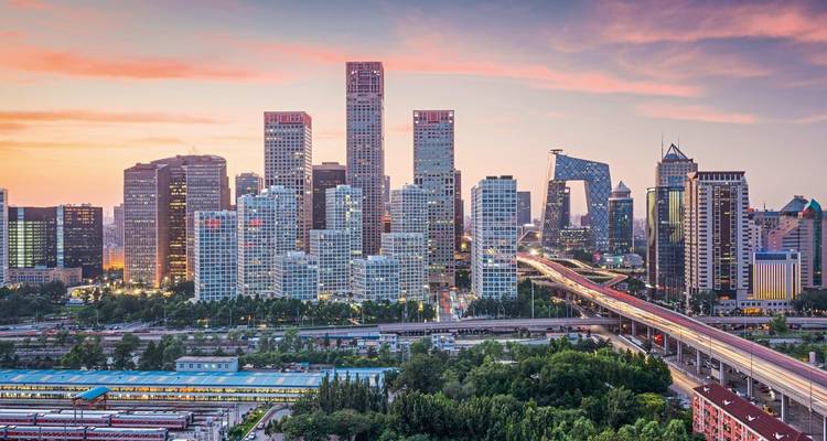 Pekings modernes Geschaeftsviertel bei Sonnenuntergang mit dem charakteristischen CCTV-Hauptquartier und zartem rosa Himmel ueber belebten Highways.
