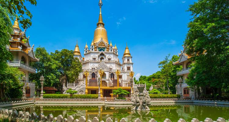 La flèche dorée de la Pagode Buu Long s'élève au-dessus de structures blanches ornées reflétées dans un étang aux lotus.