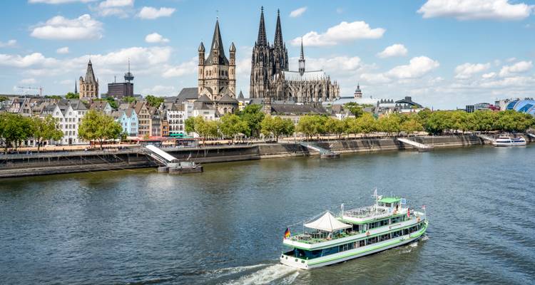 Skyline de Cologne présentant la cathédrale emblématique aux deux flèches et un bateau de croisière naviguant sur le Rhin.
