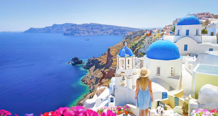 Une femme portant un chapeau de soleil contemple la mer Égée bleue et les églises blanchies à la chaux aux dômes bleus qui s'étagent le long des falaises d'Oia, à Santorin.