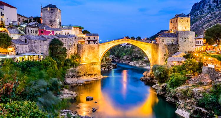 Pose longue nocturne du pont illuminé Stari Most à Mostar se reflétant dans la rivière Neretva.