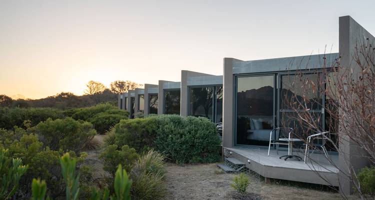Petits chalets de lodge de style moderne nichés parmi la végétation côtière au crépuscule en Tasmanie.