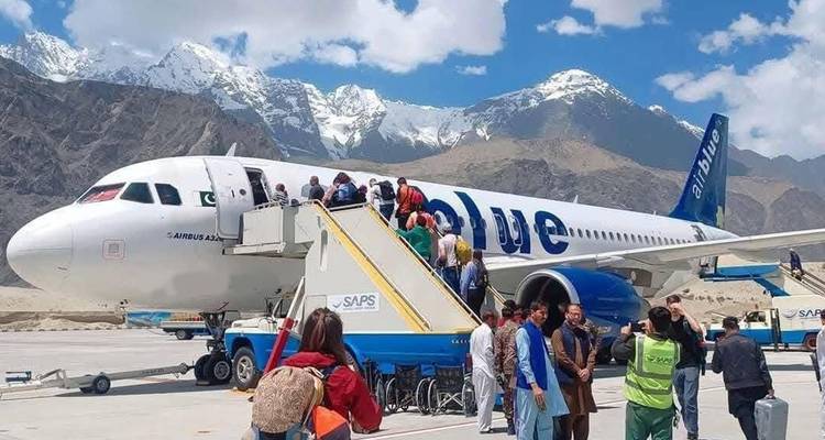 Les passagers embarquent sur un avion sur le tarmac avec des montagnes enneigées qui se dressent en arrière-plan à un aéroport situé en haute altitude.