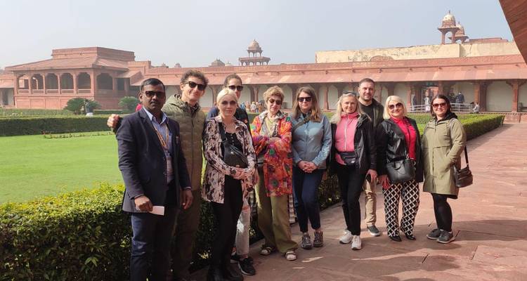 Een groep toeristen poseert in de binnenplaats van Fatehpur Sikri, omgeven door rode zandstenen gebouwen en verzorgde hagen.