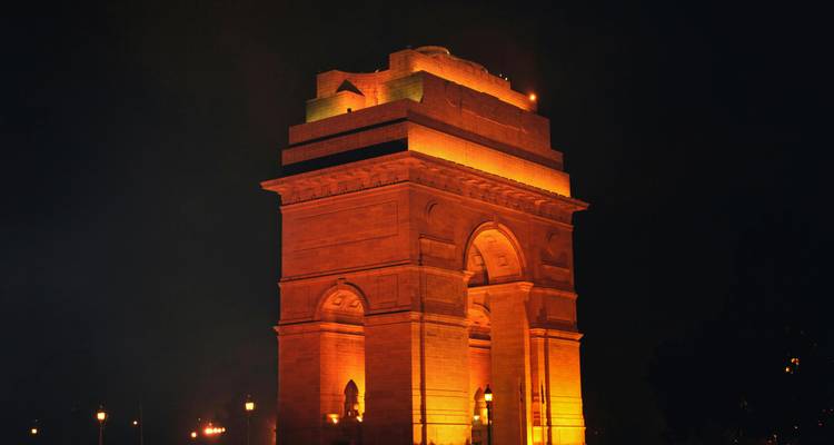 Het India Gate-monument verlicht met warme oranje lichten tegen een donkere nachtHemel.