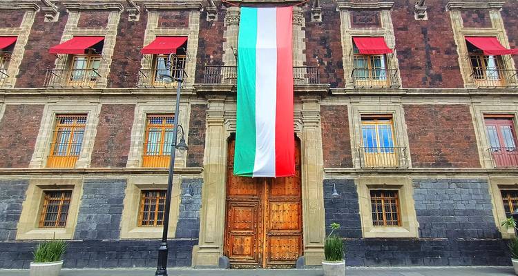 Historische Steinfassade mit einem großen vertikalen Banner in den grün-weiß-roten Farben Mexikos behängt.