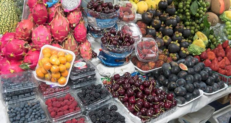 Tisch mit bunten frischen Beeren, Kirschen, Drachenfrüchten und anderen exotischen Produkten auf einem Markt aufgestapelt.