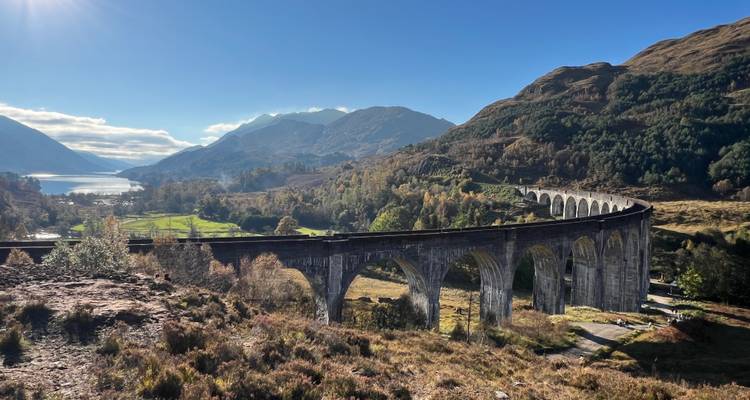 Historische Glenfinnan Viaduct die zich slingert door het Hooglanden landschap met een loch en bergen op de achtergrond.