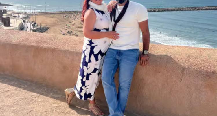 Couple souriant sur le mur d'une forteresse en bord de mer avec des vagues qui se déroulent en dessous.