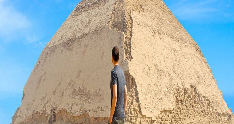 Traveler gazing up at the Bent Pyramid under a clear blue sky.