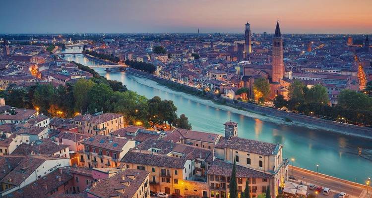 Dämmerungsluftaufnahme von Verona mit dem Fluss Etsch, der sich durch historische Dächer schlängelt, und beleuchteten Brücken.