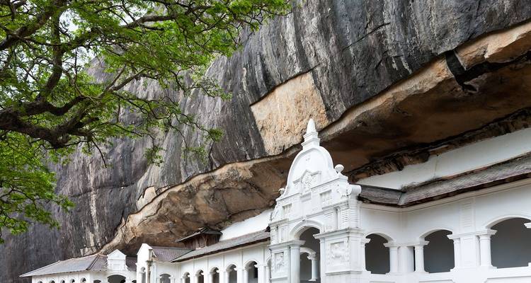 Witgekalkt gevel van het Dambulla Cave Temple-complex dat onder een enorme uitstekende rotsrotswand is gebouwd.