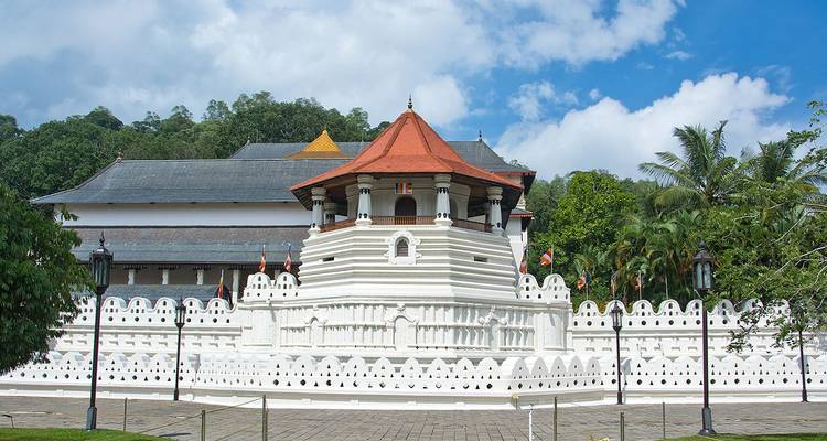 Buitenkant van de Tempel van de Heilige Tandreliek in Kandy met witte muren en een rood pannendak tegen een blauwe lucht.