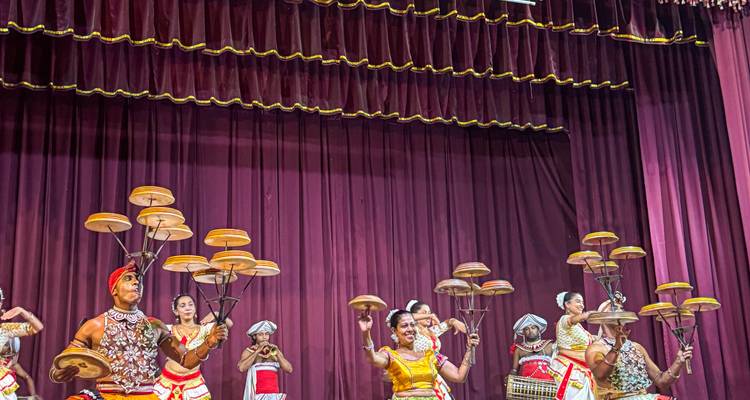Les danseurs traditionnels sri-lankais équilibrent des assiettes tournantes sur des poteaux lors d'une représentation scénique colorée avec des rideaux bordeaux.