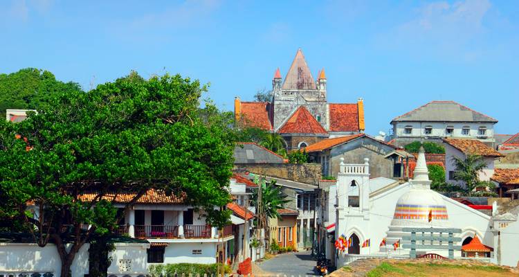 Un mélange d'églises coloniales, de toits carrelés et d'arbres verdoyants bordent une rue tranquille à l'intérieur du fort de Galle sous un ciel dégagé.