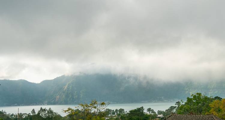 Les nuages bas s'étirent sur les montagnes lointaines qui bordent un vaste lac sous un ciel gris.