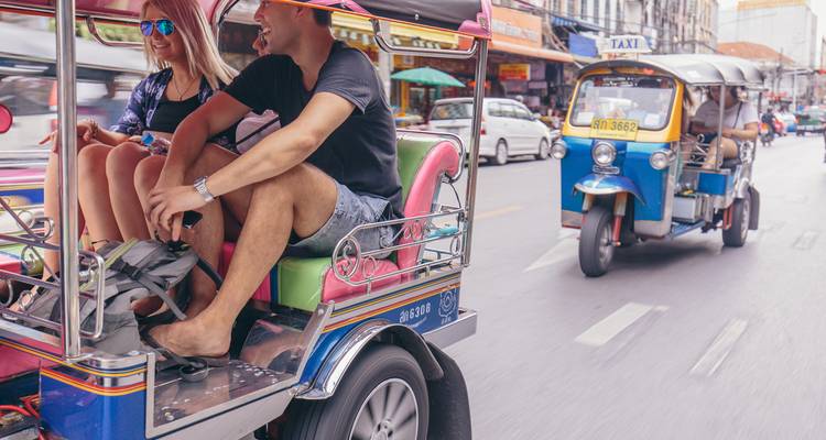 Travellers ride in a colorful tuk-tuk through busy city streets while another tuk-tuk follows.