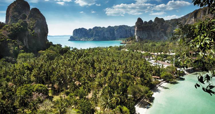 Panoramic view over emerald sea, jungle palms and towering limestone cliffs on a tropical peninsula.