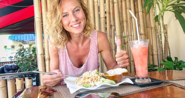 Traveller enjoys a plate of fried rice and a fruit smoothie at an open-air café with bamboo décor.