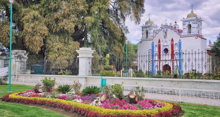 Kleurrijke bloemenbedden en een schilderachtig koloniaal kerkje achter smeedijzeren hekken in Santa María del Tule.