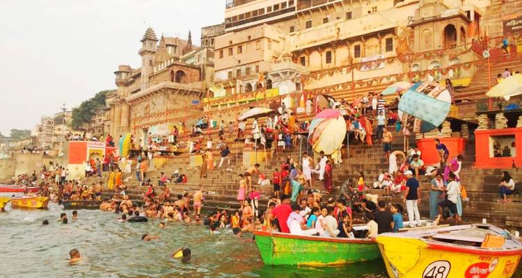 Geschäftige Tagesszene an den Varanasi-Ghats mit Pilgern, die baden, und bunten Booten auf dem Ganges-Fluss.