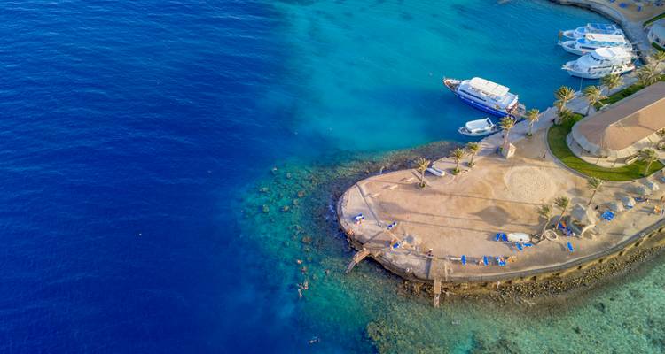 Luchtfoto van een turquoise baaitje in de Rode Zee met een klein jachthaventje, zandbank en aangemeerde boten.
