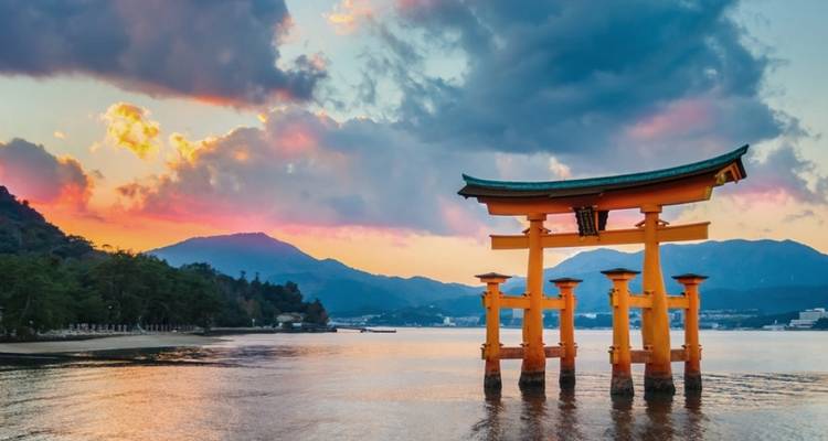 Ikonisches, auf dem Wasser schwebendes Torii-Tor des Itsukushima-Schreins, das sich vor einem dramatischen Himmel bei Sonnenuntergang abzeichnet