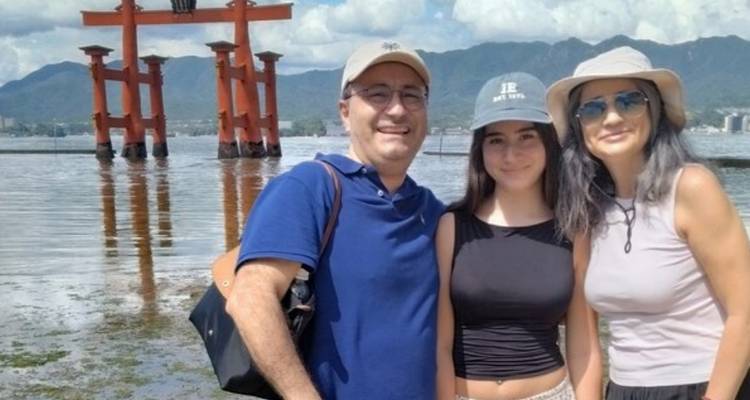 Familie poseert bij de beroemde rode torii-poort die in zee staat met bergen op de achtergrond.