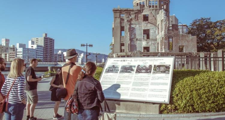 Een begeleide groep leest informatiegegevens bij de ruïnes van de A-Bom Koepel langs de rivieroevers van Hiroshima.