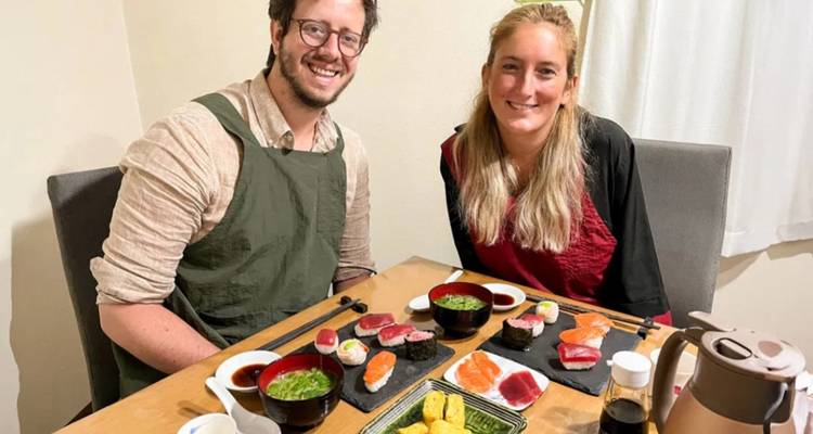 Een glimlachend stel zit aan een tafel met kleurrijke nigiri en miso soep tijdens een sushi-les.