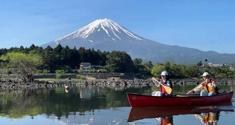 Twee peddeleers varen met hun kano over een rustig meer met de Berg Fuji die zich perfect in het water spiegelt.