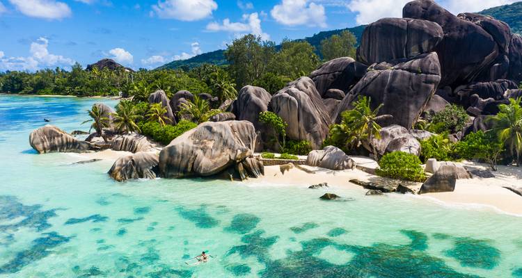 Eine kristallklare türkisfarbene Lagune und dramatische Granitfelsen säumen einen weißen Sandstrand auf den Seychellen, darunter ein einsamer Schnorchler.